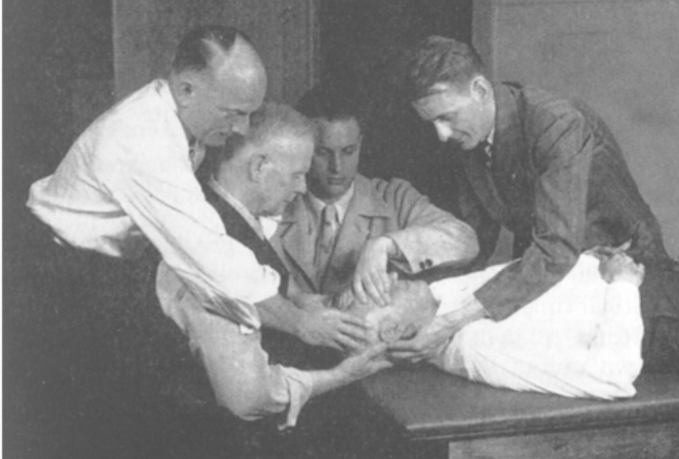 Vier Männer behandeln einen auf einem Tisch liegenden Mann am Kopf